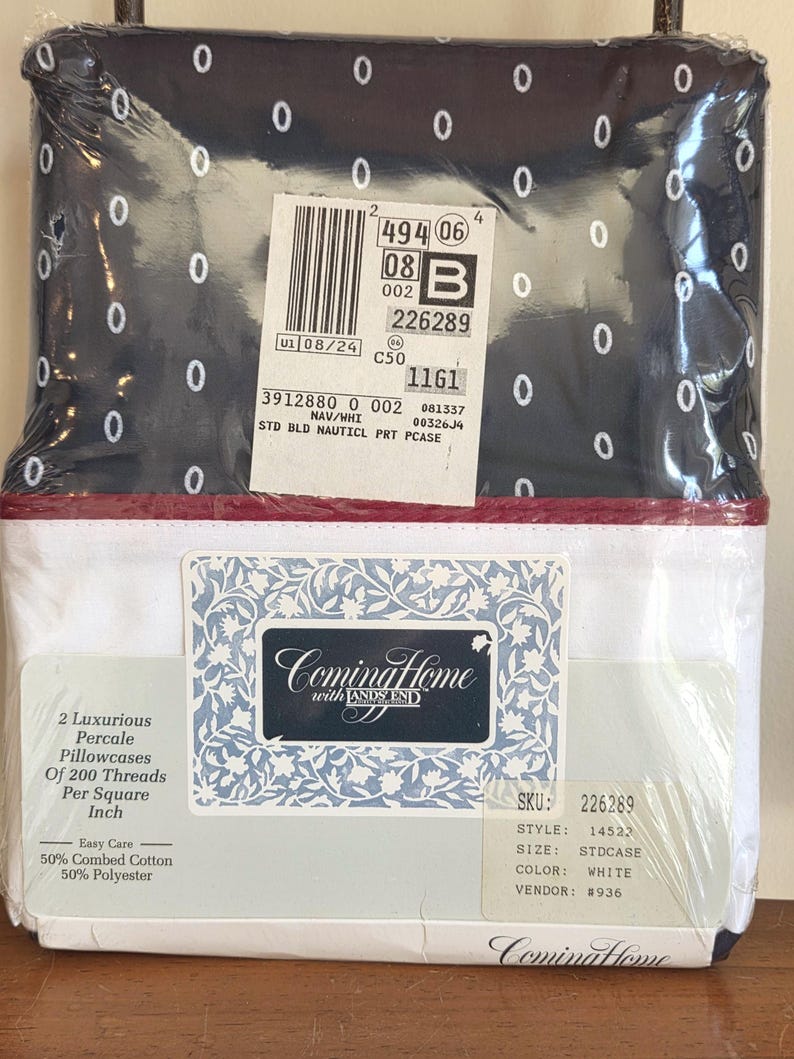 May include: A packaged set of Coming Home with Lands' End pillowcases. The top portion of the package features a navy blue fabric with white oval patterns. The bottom portion is white with a red border. The package includes two percale pillowcases.