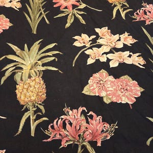 Könnte beinhalten: Schwarzer Stoff mit einem sich wiederholenden Muster aus tropischen Blumen und Ananas. Die Blumen sind rosa und weiß, und die Ananas sind gelb. Grüne Blätter und Stiele vervollständigen das Design.