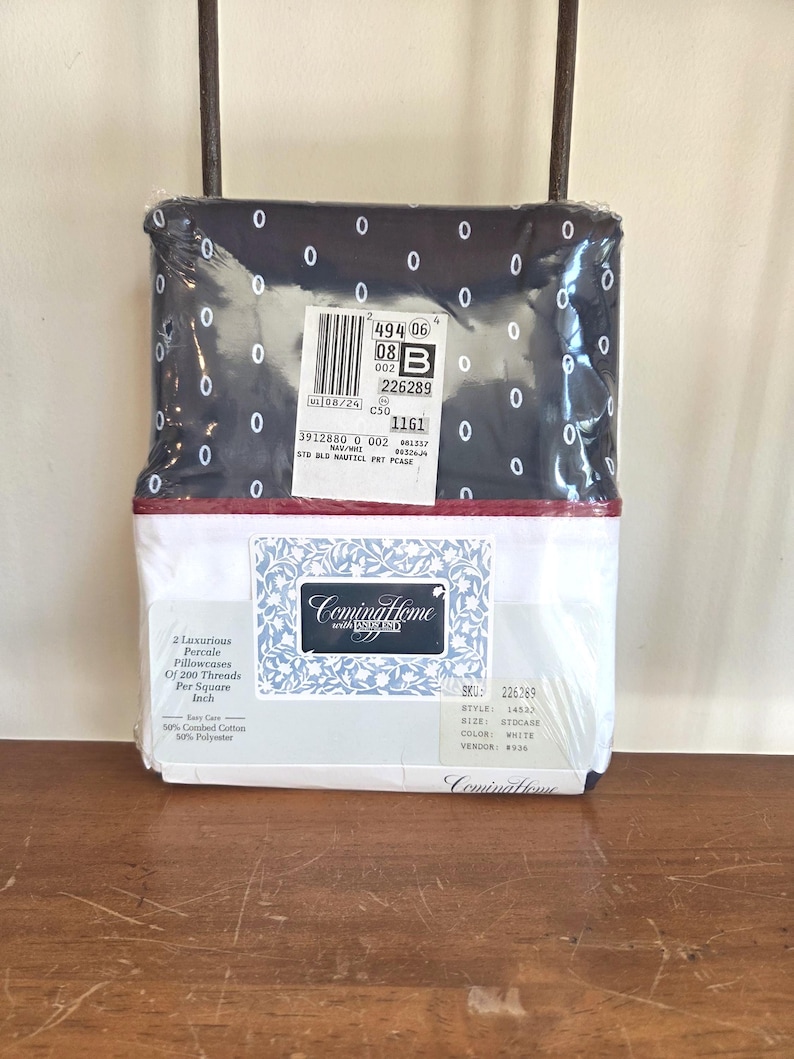 May include: A packaged bedding set featuring a navy blue top sheet with white oval patterns and a white bottom sheet. The packaging includes a label with product information and the brand name "Coming Home". The set includes two percale pillowcases.