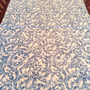 K&ouml;nnte beinhalten: Wei&szlig;e Tischdecke mit einem blauen und wei&szlig;en Blumenmuster. Das Muster zeigt komplizierte Wirbel und Bl&auml;tter.