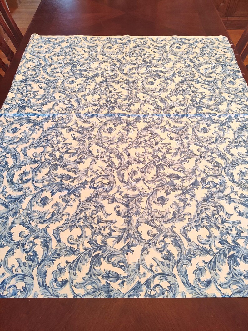 K&ouml;nnte beinhalten: Wei&szlig;e Tischdecke mit einem blauen und wei&szlig;en Blumenmuster. Das Muster zeigt komplizierte Wirbel und Bl&auml;tter.