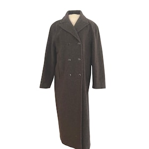 May include: A long, dark charcoal gray wool-blend coat featuring a double-breasted front closure with six visible buttons, a notched lapel collar, and long sleeves. The coat has a straight, structured silhouette that extends to the lower calf.