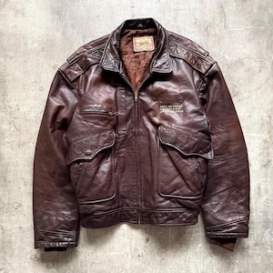 Puede incluir: Chaqueta bomber de cuero marrón desgastado con cremallera, dos bolsillos delanteros y un pequeño bolsillo en el pecho. La chaqueta presenta detalles acolchados en los hombros y el texto "PARA WING FORCE" en el pecho.