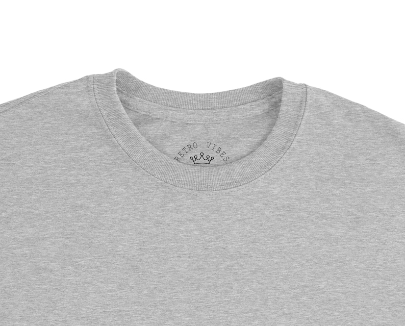 May include: A heather gray crew neck t-shirt. The shirt features the text "RETRO VIBES" with a crown graphic printed on the neckline. The t-shirt is made of a soft, comfortable material.