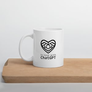 May include: White ceramic mug featuring a black heart design and the words "in love with ChatGPT". The mug is placed on a wooden surface.