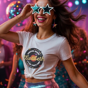 May include: A woman wearing star-shaped sunglasses and earrings, a white t-shirt with a graphic that says "Dancing Queen Elisabeth It's My Party Time", and a shiny, iridescent skirt. The background is a colorful party scene with a disco ball.
