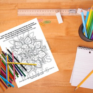 May include: A coloring page with a mandala design, surrounded by colored pencils, a notepad, and a pencil. The page has text that reads, "Color this design to show what feelings you have today." A ruler and paperclips are also visible.
