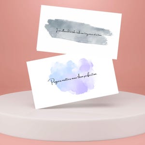 May include: Two white cards with inspirational quotes and watercolor backgrounds. The top card has a gray watercolor background and the quote "I am allowed to take my time, one tiny piece at a time". The bottom card has a blue and purple watercolor background and the quote "Progress matters more than perfection".