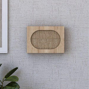 May include: A rectangular wooden wall shelf with an oval cutout, filled with a tan fabric. The shelf is mounted on a textured, light gray wall. A framed picture and a plant are visible in the background.