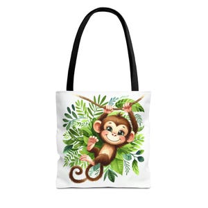 May include: White tote bag with a black handle. It features a cartoon monkey hanging from a rope surrounded by green leaves. The monkey is brown and smiling. The bag is designed for carrying items.
