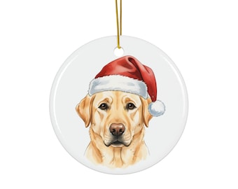 May include: A circular Christmas decoration with a watercolour illustration of a yellow Labrador Retriever wearing a red Santa hat with white trim and a white bobble. A gold string is attached for hanging.