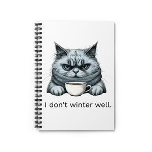 May include: Spiral-bound notebook with a white cover featuring a grumpy gray cat wearing a scarf and holding a coffee cup. The text "I don't winter well" is printed below the cat illustration.