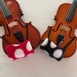 May include: Two violins with black and white polka dot fabric covers. The violin on the left has a red cover with white polka dots. The violin on the right has a black cover with white polka dots.