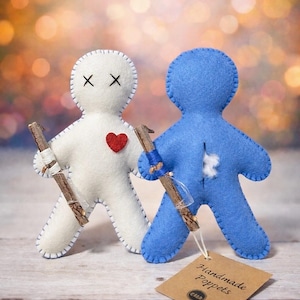 May include: Two handmade felt poppets, one white and one blue, stand side-by-side. The white poppet has stitched black eyes and a red heart. Both hold small sticks wrapped with twine. A tag reads "Handmade Poppets."