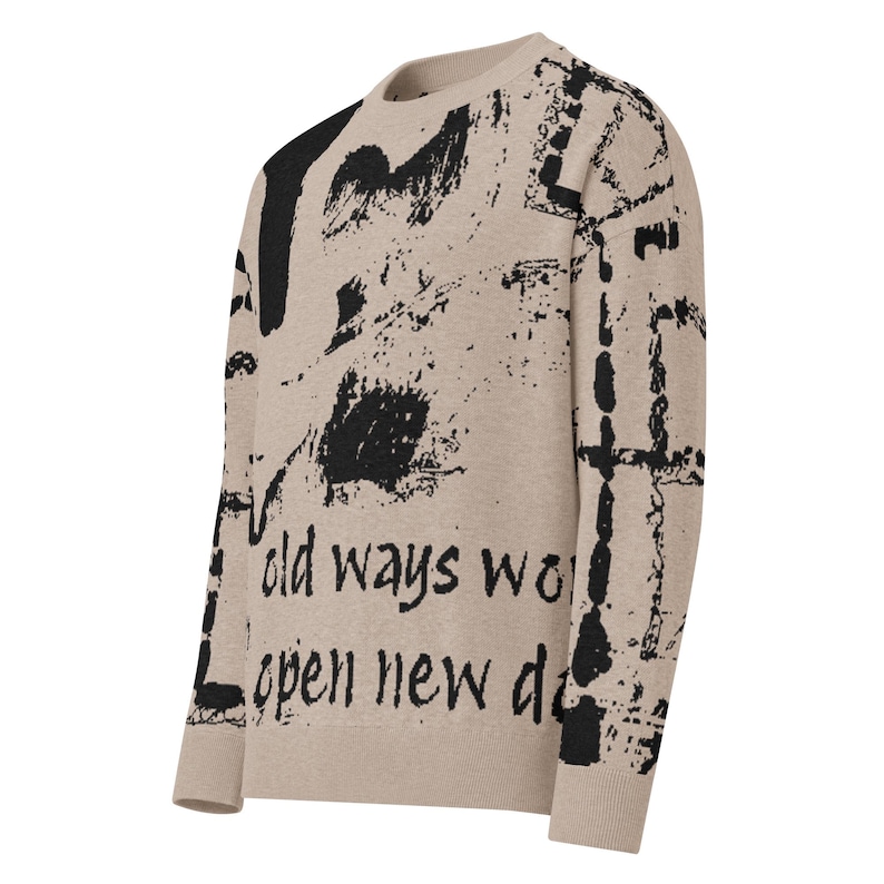 May include: Beige sweater featuring black abstract paint strokes and the text "old ways wo open new d". The sweater has a crew neck and long sleeves. The design covers the front and sleeves.