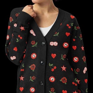 May include: Black cardigan sweater with a V-neck and button closure. The sweater is adorned with red hearts, roses, cherries, stars, dice, and billiard balls. The sweater is a dark color and has a white undershirt.