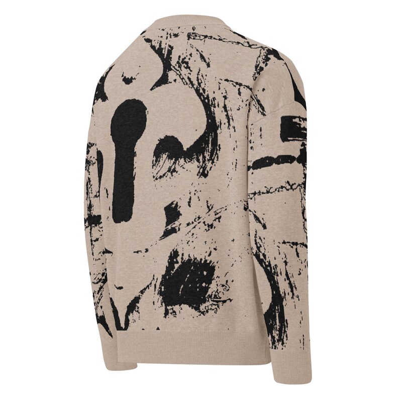 May include: Beige sweater featuring a black keyhole and abstract brushstroke design. The long-sleeved sweater has a crew neck and ribbed cuffs and hem. The back of the sweater is visible, showcasing the bold, artistic pattern.