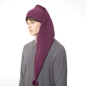 May include: A deep purple, long-tailed hat with a small pom-pom at the end. The hat is made of a soft material and is designed to be worn on the head. The hat is a whimsical accessory.