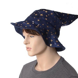 May include: A dark blue wizard hat featuring a gold foil star and celestial pattern. The hat has a wide, slightly drooping brim and a pointed, curved top section. The fabric appears to have a soft, velvet-like texture throughout the entire surface.
