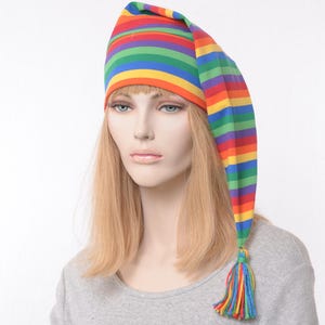 May include: A colorful, striped nightcap in a rainbow of colors: red, orange, yellow, green, and blue. The hat has a long, pointed shape with a tassel at the end. The tassel is made of multiple strands of colorful thread.