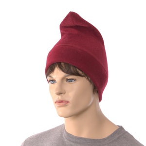 May include: A maroon beanie with a pointed top. The beanie is made of a soft, knitted fabric.