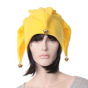 May include: A bright yellow jester hat with three pointed tips and gold bells. The hat is made of a soft fabric and is worn by a mannequin. The hat is a costume accessory.