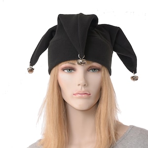 May include: A black fleece hat featuring three distinct pointed sections that hang down. Each of the three points is adorned with a small, metallic silver-toned bell attached by a circular ring, creating a jester-inspired headwear design.