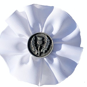 May include: A white fabric flower with a silver button featuring a thistle design.
