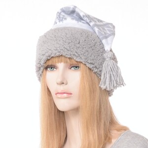 May include: A gray winter hat with a white snowflake pattern on the pointed top. The hat has a fluffy, textured brim and a matching tassel. The hat is designed for cold weather and is made of soft materials.