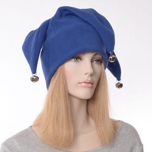 May include: A royal blue jester hat with three pointed tips, each adorned with a small silver bell. The hat is made of a soft fabric and is worn by a mannequin with blonde hair.