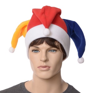 May include: A colorful jester hat with red, blue, and yellow points, a white brim, and white pom-poms. The hat is worn by a mannequin. This festive hat is perfect for costume parties and theatrical performances.
