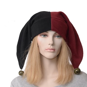 May include: A two-toned jester hat featuring a split design with one side in solid black and the other in deep burgundy. The hat has two long, drooping points, each finished with a small, round, metallic brass-coloured bell at the tip.