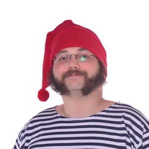 May include: A man wearing a red fleece sleeping cap with a white pom-pom and a striped shirt.