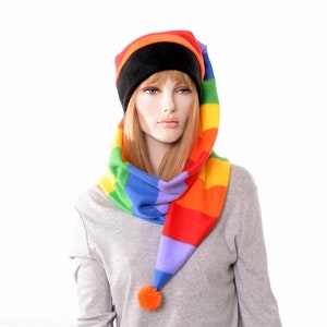 May include: A rainbow-striped hat and scarf set. The hat has a black band and a long, pointed end with an orange pom-pom. The scarf is a matching rainbow pattern. The set is displayed on a mannequin.