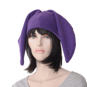 May include: A purple fleece hat with long, floppy ears. The hat is a vibrant shade of purple and is designed to cover the head and ears. The hat is shown on a mannequin.