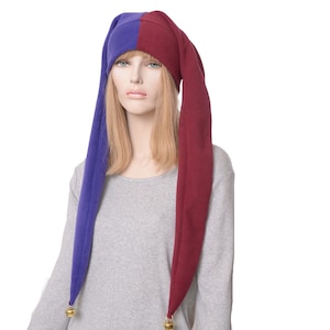 May include: A purple and burgundy fleece hat with long tails and gold bells at the ends. The hat is worn by a person with long blonde hair.