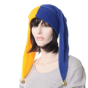 May include: A jester hat with a yellow and blue color scheme. The hat has long, pointed ends with small gold bells attached. The hat is worn by a mannequin with short black hair and a gray shirt.