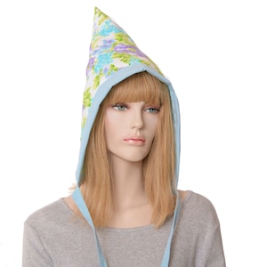 May include: A floral print bonnet with a pointed top and a light blue trim. The bonnet features a pattern of blue, purple, and green flowers on a white background. Light blue ties hang down from the bonnet.
