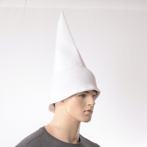 May include: A plain white pointed hat with a tall, conical crown and a slightly flared brim. The hat is constructed from a smooth, solid white fabric and features a structured, upright shape that tapers to a rounded point at the very top.