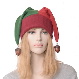 May include: A jester hat with a green and burgundy color scheme. The hat has a rounded crown and long, pointed tips. Brown acorn-shaped ornaments dangle from the tips. The hat is made of a soft fabric and is designed for costume or novelty wear.