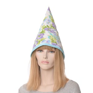 May include: A cone-shaped hat with a floral pattern in shades of purple, green, and blue on a white background. The hat is trimmed with a light blue border. The hat is worn by a mannequin.