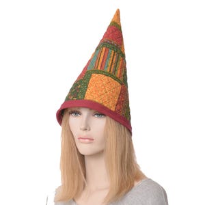 May include: A red, green, orange, and yellow patchwork fabric cone-shaped hat. The hat has a red brim and is worn by a person with long blonde hair.
