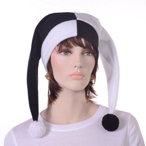 May include: A black and white jester hat with a checkered crown and long, pointed ends. Each end has a matching pom-pom. The hat is worn by a mannequin. The hat is made of a soft material.