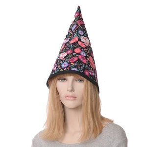 May include: A black pointed hat with a floral print featuring pink, red, and blue flowers. The hat is worn by a person with long blonde hair.