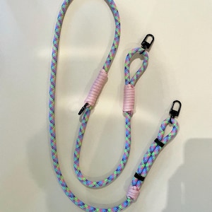 May include: A multi-colored rope leash with black metal clasps. The leash features a pastel rainbow pattern of blue, green, and purple. The leash has pink accents and is designed for pet use.