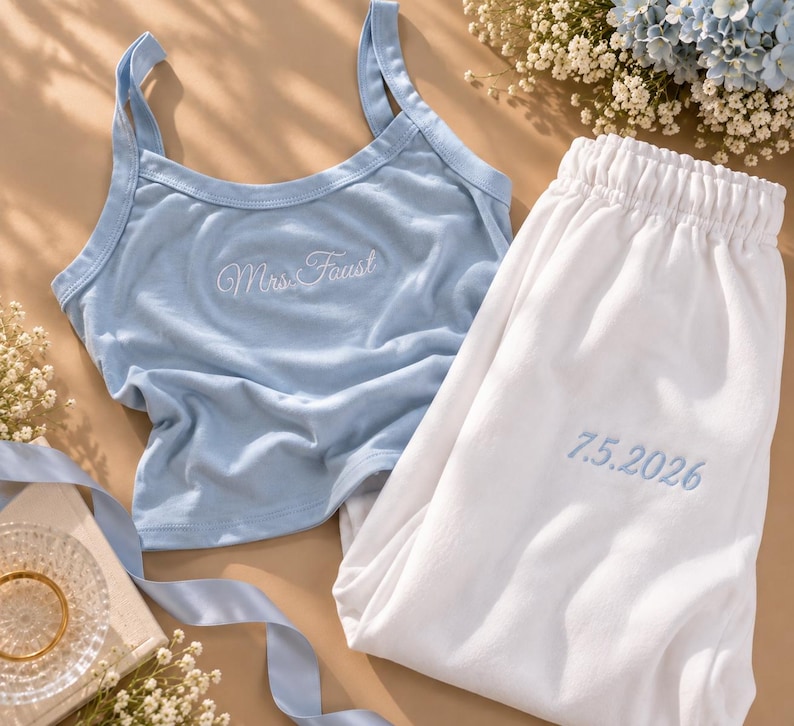 May include: A light blue tank top with white embroidery reading Mrs. Faust and white pajama pants with light blue embroidery reading 7.5.2026. The set features a scoop neckline, thick straps, and an elastic waistband on the pants.
