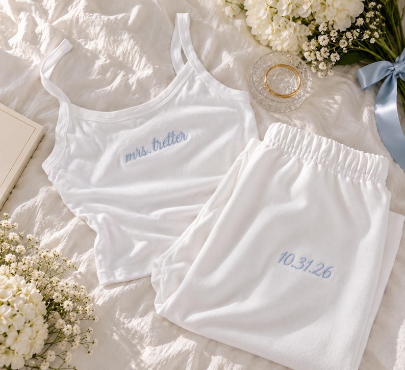 May include: A white pajama set consisting of a tank top and elastic-waist pants. The tank top features the embroidered blue text "mrs. tretter" on the chest, and the pants feature the embroidered blue date "10.31.26" on the upper leg area.