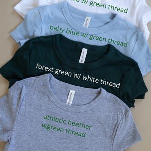 a collection of four t-shirts, each with a different color and thread pattern, arranged in a row.