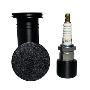 Può includere: Set di cappuccio e stivale per candela neri con una candela. La candela ha un isolante in ceramica bianco e il testo "B7HS". Lo stivale e il cappuccio sono neri e cilindrici.