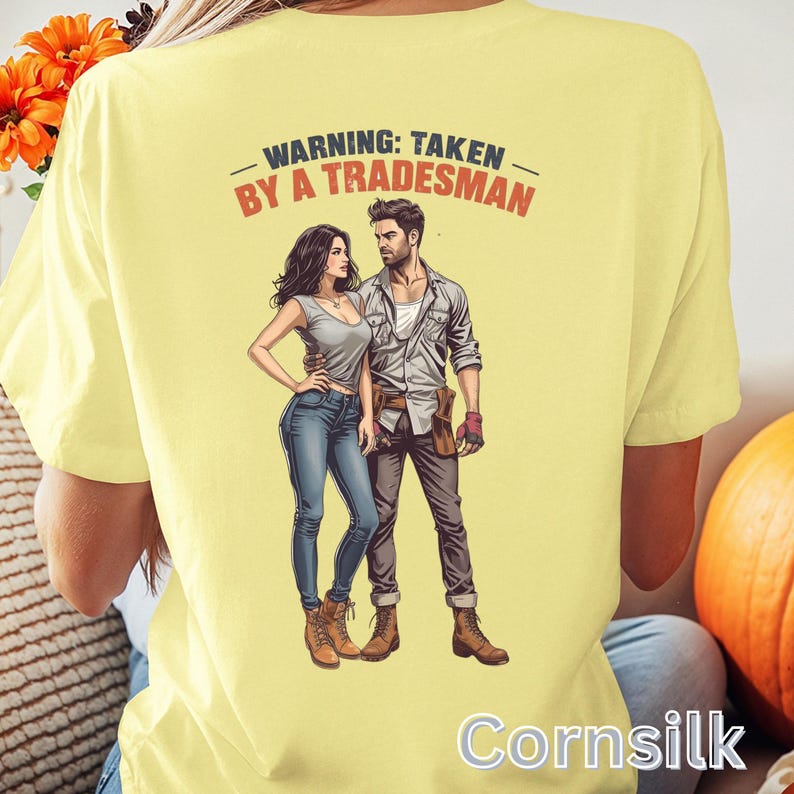 K&ouml;nnte beinhalten: Hellgelbes T-Shirt mit dem Text "WARNING: TAKEN BY A TRADESMAN" &uuml;ber einer Illustration eines Paares. Die Illustration zeigt einen Mann und eine Frau in Freizeitkleidung. Das Wort "Cornsilk" ist unten auf dem T-Shirt aufgedruckt.
